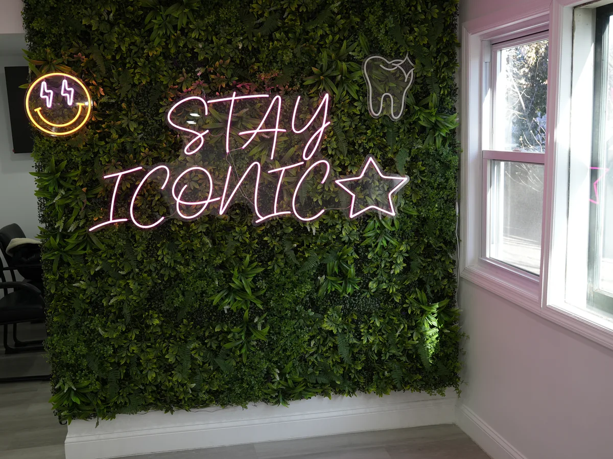 Green plant wall with a pink STAY ICONIC neon sign in the Freeport office