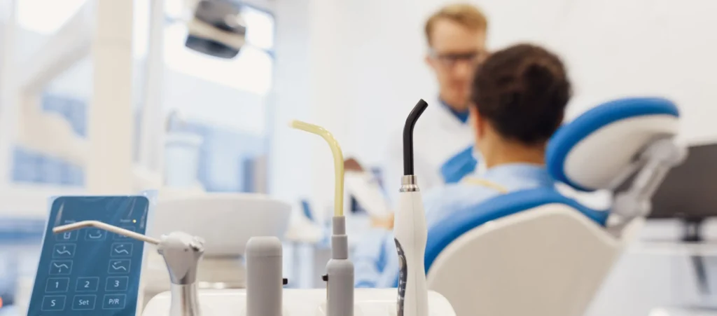 Dentist with a patient in a dental chair, with focus on dental equipment in the foreground.